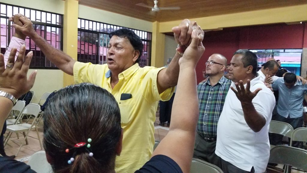 Men with joined hands raised in fervent prayer during a church gathering in Panama