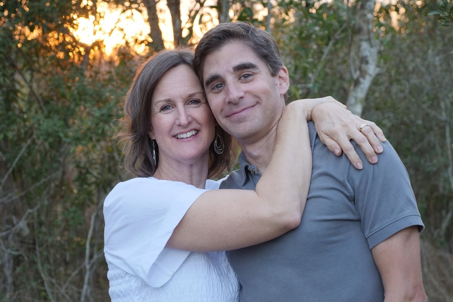Chris and Rebecca Vennetti smiling with their arms around each other outdoors at sunset
