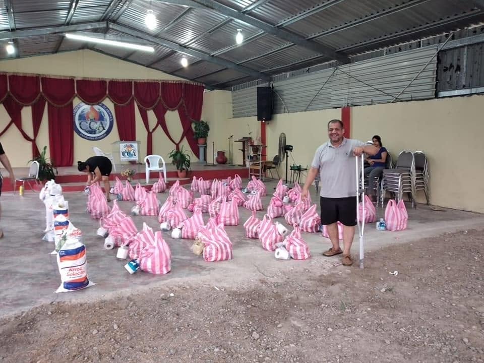 Rows of food parcels laid out in a church hall before an outreach, with a volunteer standing beside them