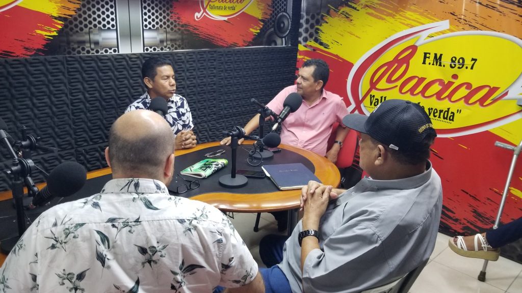 Four men sit around a table of microphones in a Colombian radio studio, talking together on air.