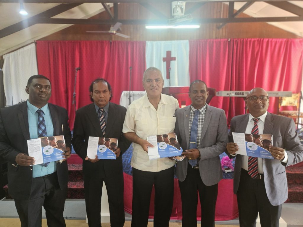 Five Fijian pastors stand at the front of a church holding copies of the national prayer guide.