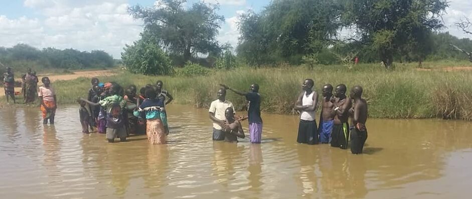 New believers wade into a river with a pastor for baptism while others watch from the bank.