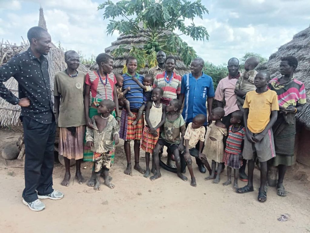 A pastor stands with families and children outside their thatched homes in a Kotido village.